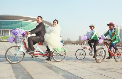氣球和鮮花裝點(diǎn)的雙人自行車，新郎郝幸福載著美麗新娘回家。