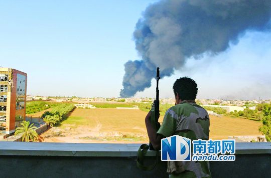 2日，利比亞首都的黎波里，一民兵武裝成員眺望被火箭彈擊中的儲(chǔ)油罐冒出濃煙。