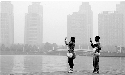 29日中午，鄭東新區(qū)如意湖畔，兩個(gè)年輕人拍攝霧霾中的景色。 鄭州晚報(bào)記者 馬健 圖