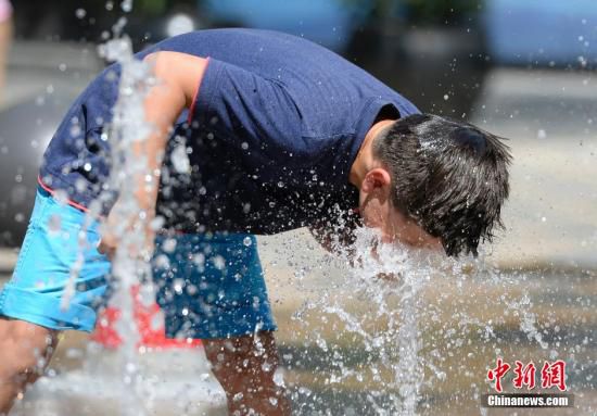 5月29日，一名小孩將頭伸向北京街頭的噴泉以降溫祛暑。