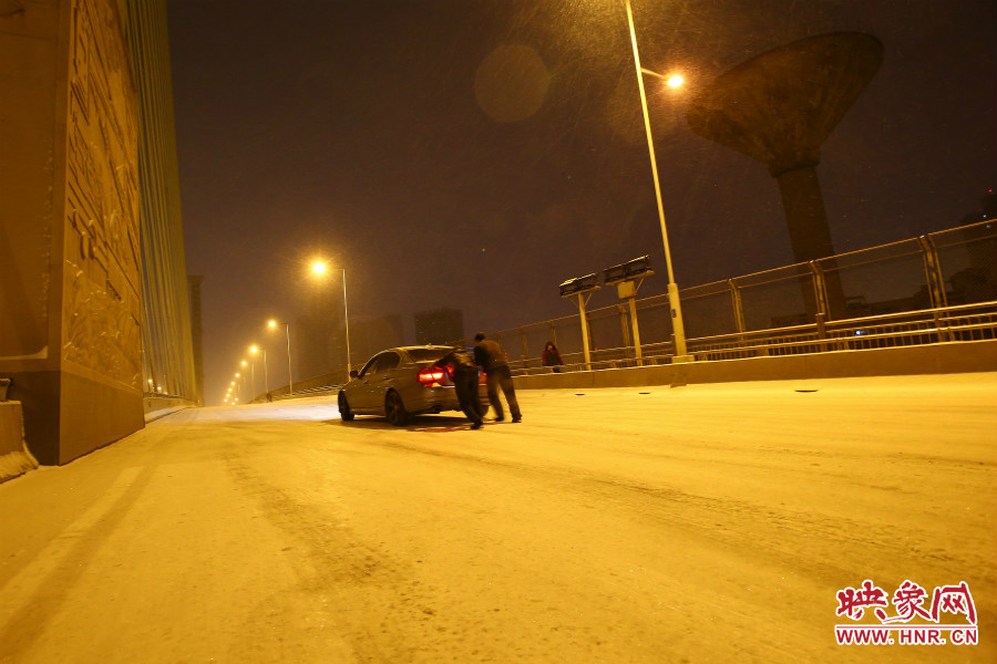 雪天路滑，汽車上橋打滑，兩名“推車人”幫助一輛私家車上坡。