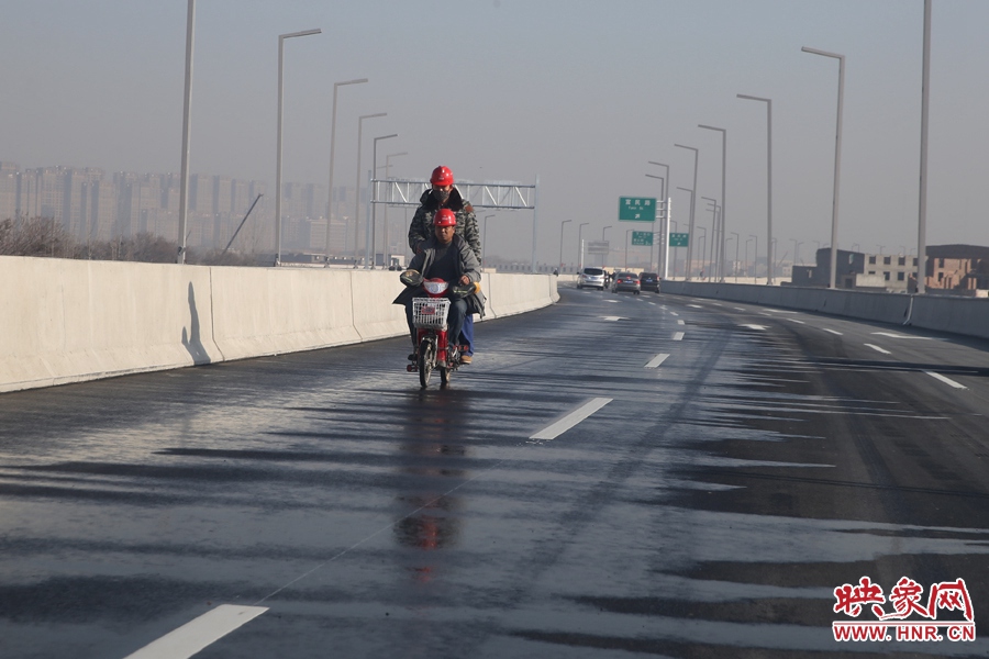 兩名工人騎車經(jīng)過灑水養(yǎng)護路面。